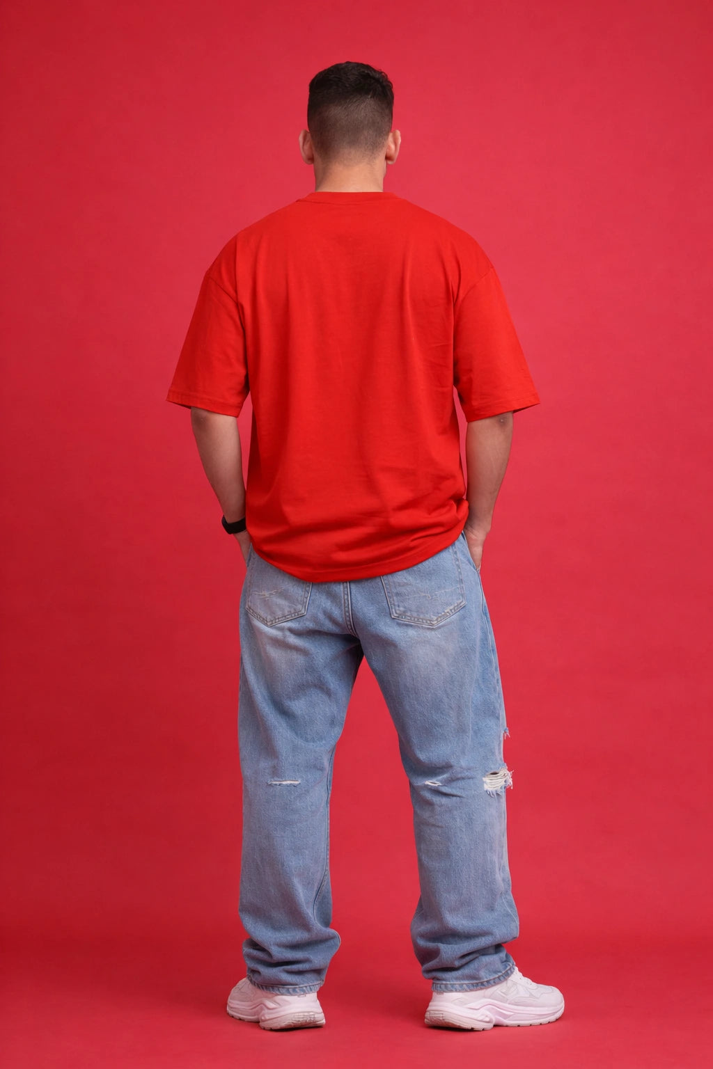 Person wearing a red t-shirt and blue jeans standing against a red background