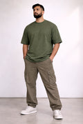 Man wearing an olive green t-shirt and cargo pants standing against a white background