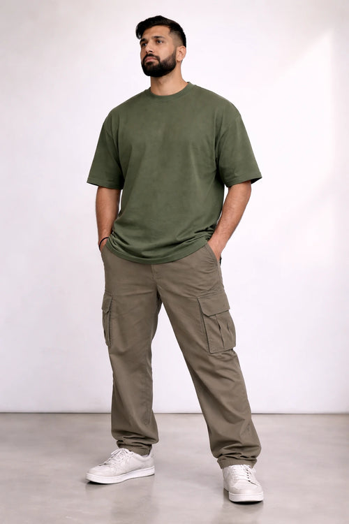 Man wearing an olive green t-shirt and cargo pants standing against a white background