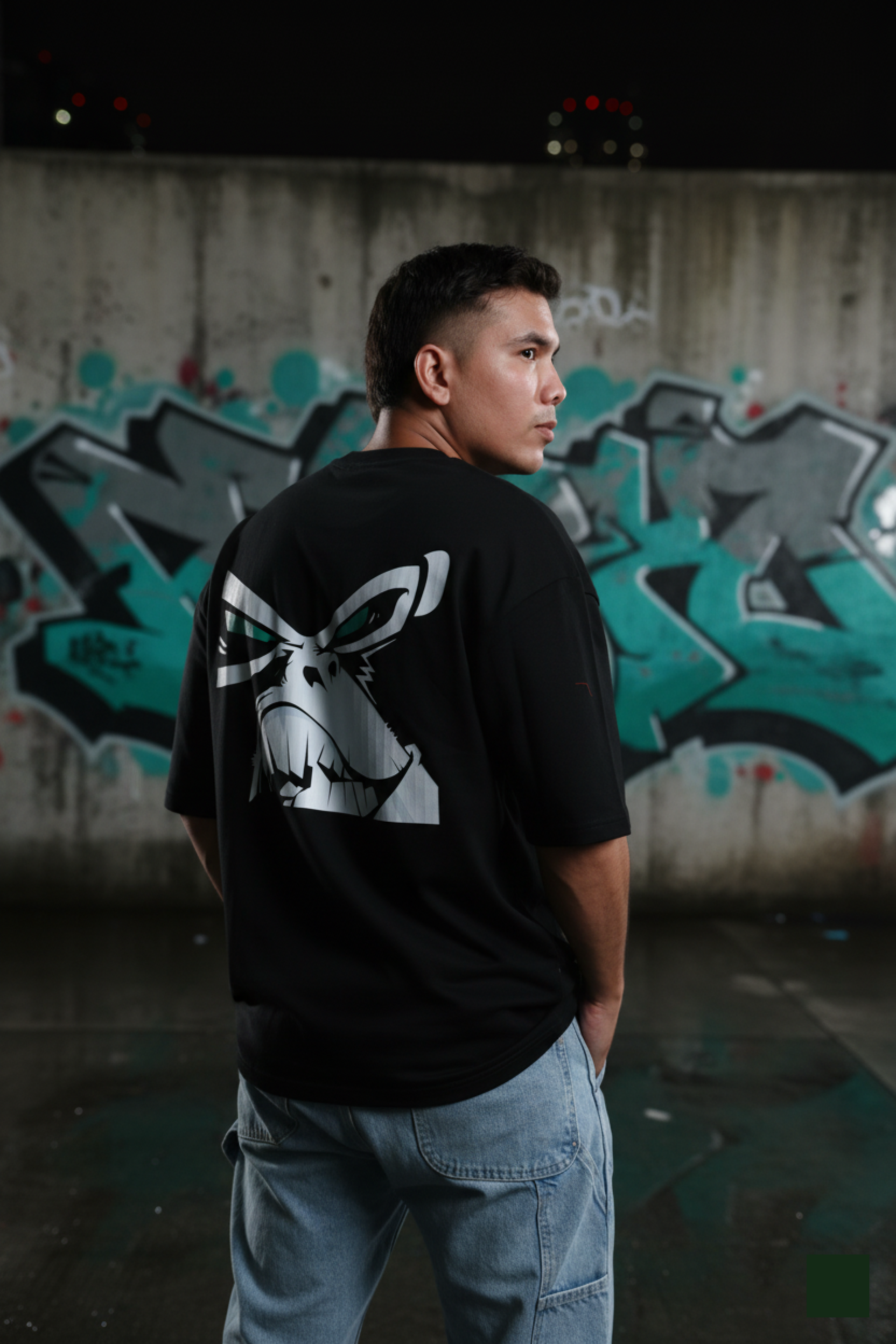 Person wearing a black t-shirt with a white graphic design in front of a graffiti-covered wall.