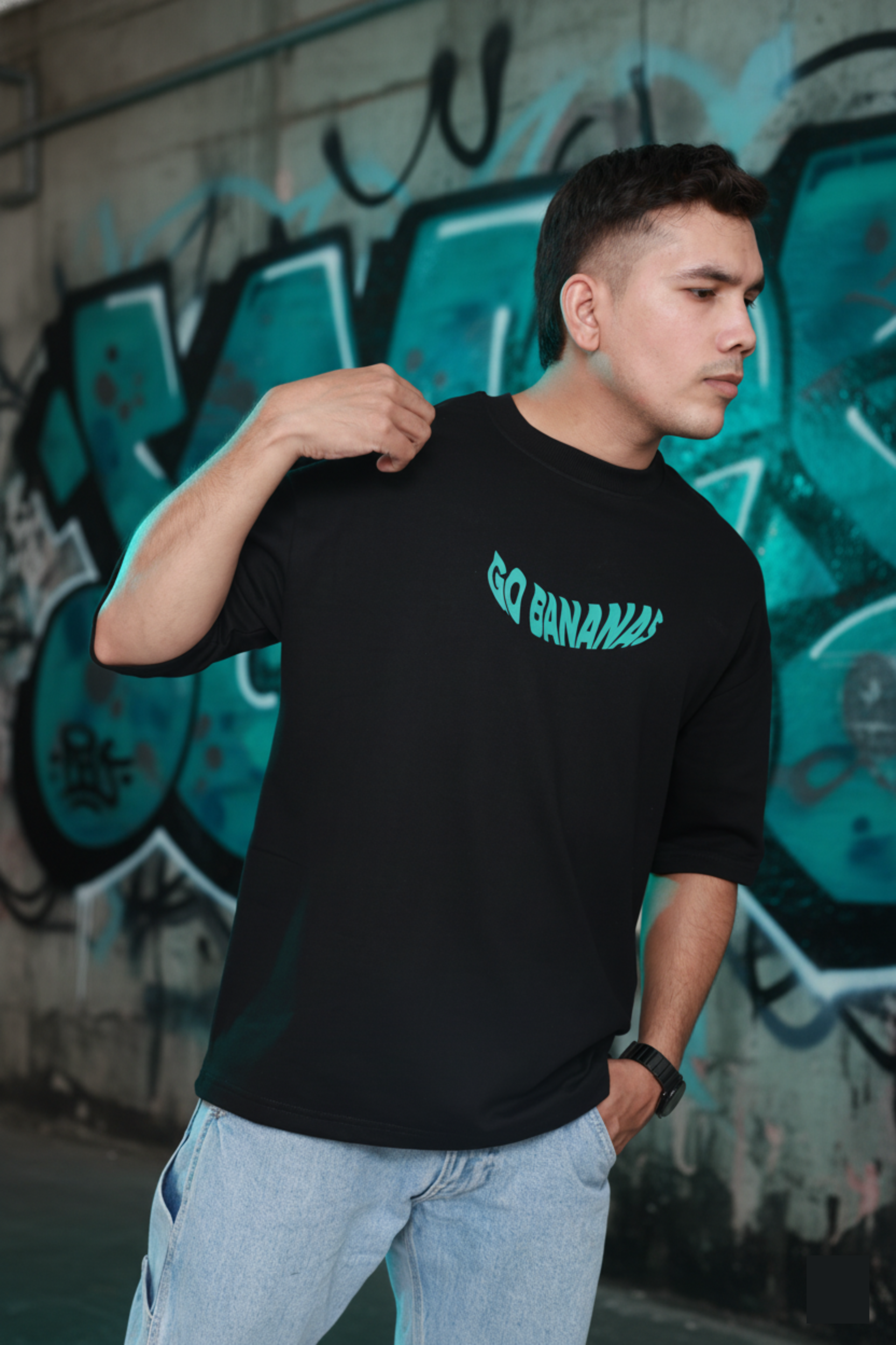 Person wearing a black t-shirt with 'GO BANANA!' text in front of a graffiti wall.