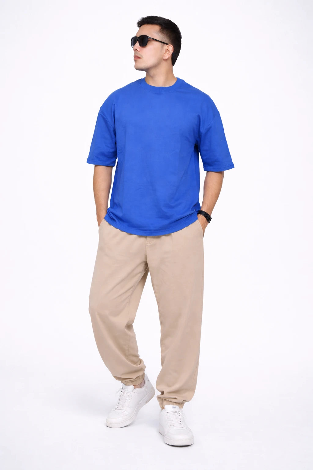 Man wearing a blue t-shirt, beige pants, and white sneakers on a white background