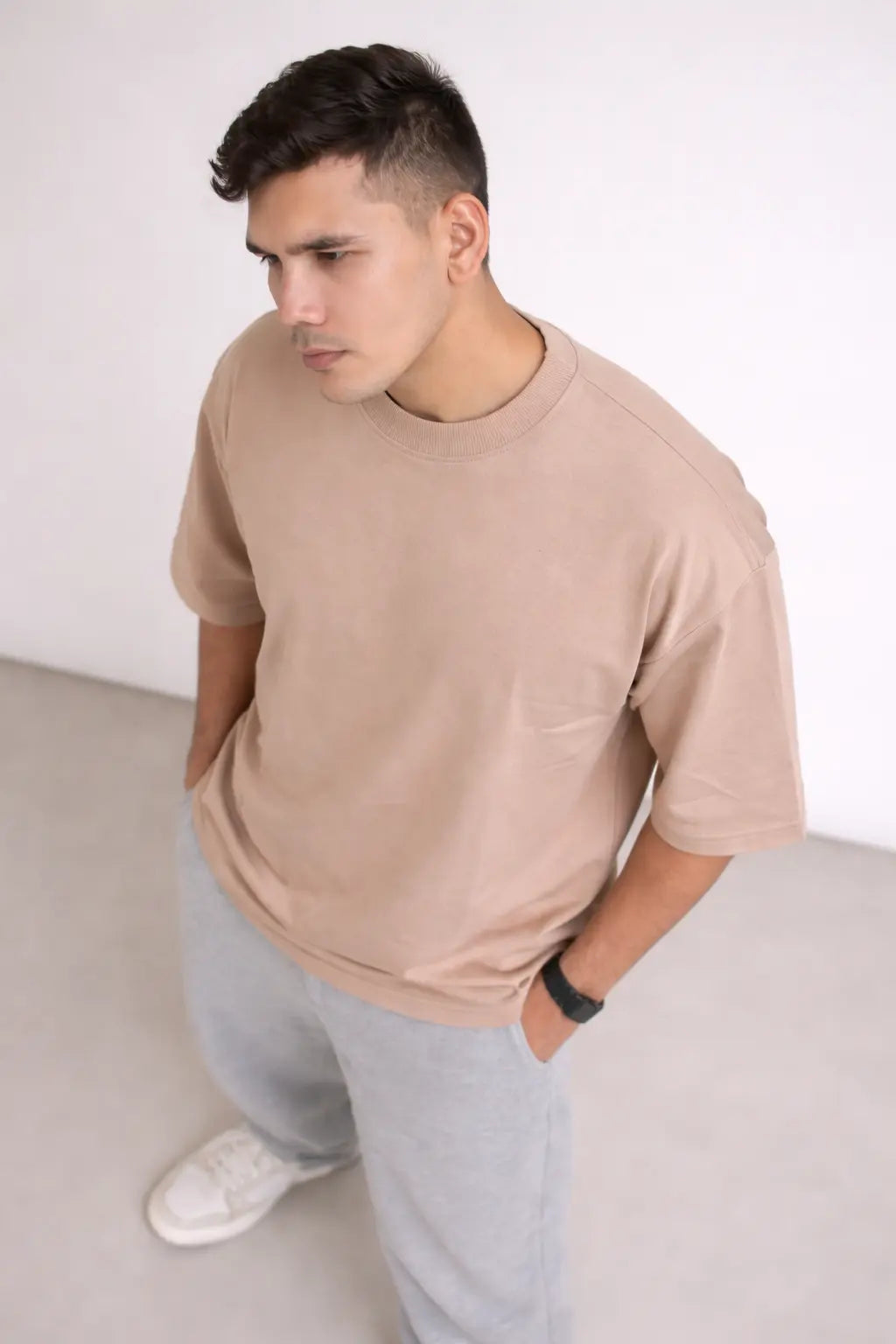 Man wearing a beige t-shirt and light gray pants against a white background