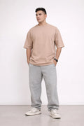 Man wearing a beige t-shirt and gray sweatpants standing against a white background