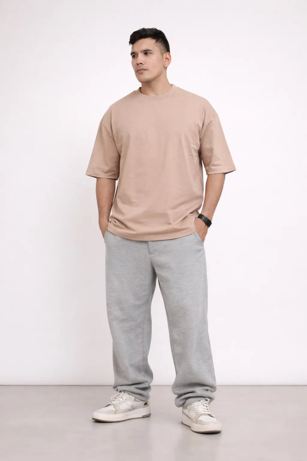 Man wearing a beige t-shirt and gray sweatpants standing against a white background