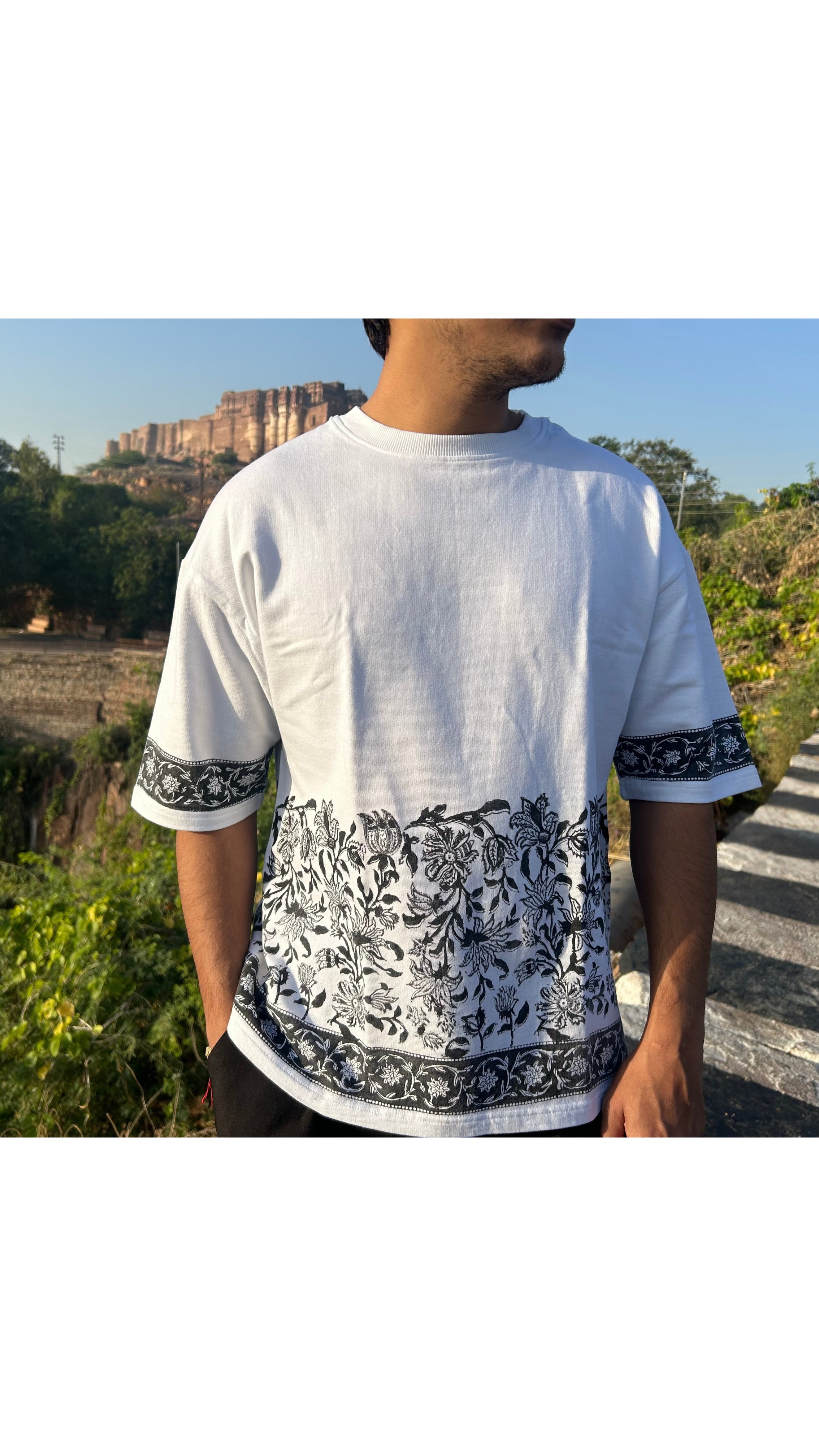 Person wearing a white t-shirt with black floral patterns in an outdoor setting.