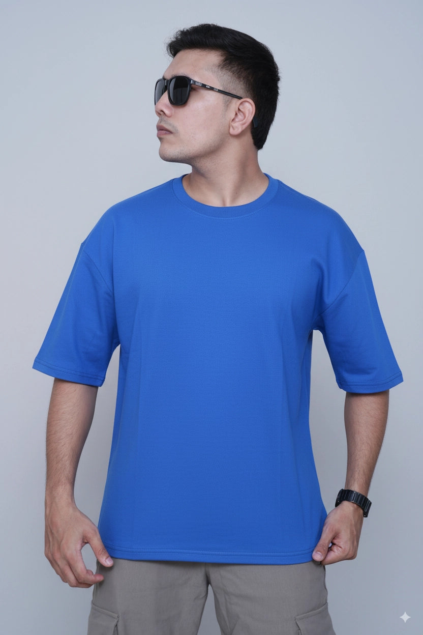 Man wearing a oversized royal blue t-shirt and sunglasses against a light gray background