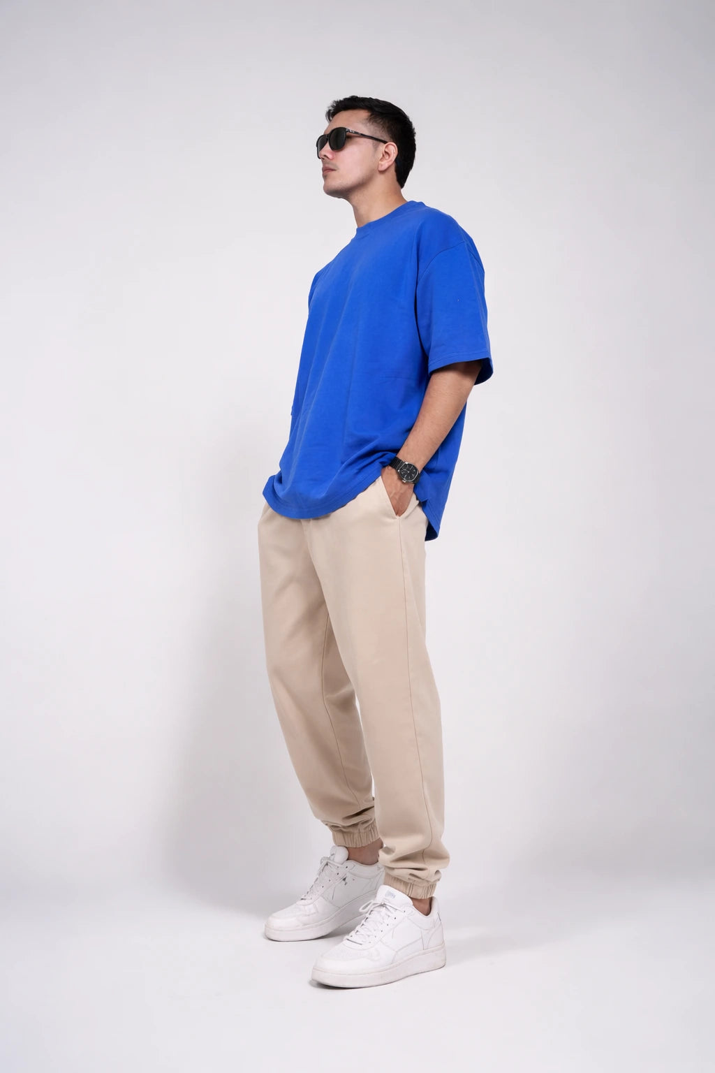 Man wearing a blue t-shirt, beige pants, and white sneakers on a white background