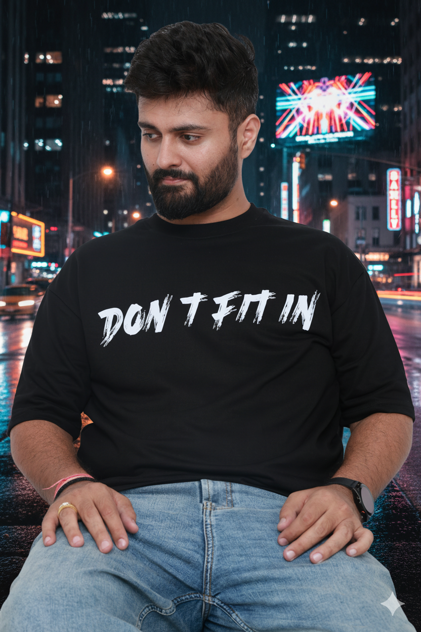 Man wearing a black t-shirt with 'DON'T FIT IN' text in an urban night setting.