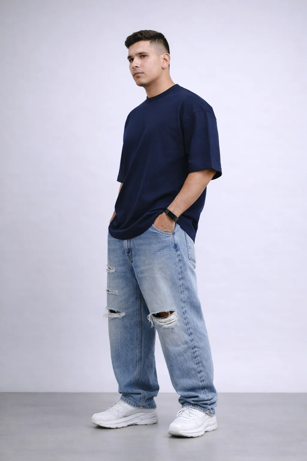Man wearing a navy t-shirt and light blue jeans with a white background