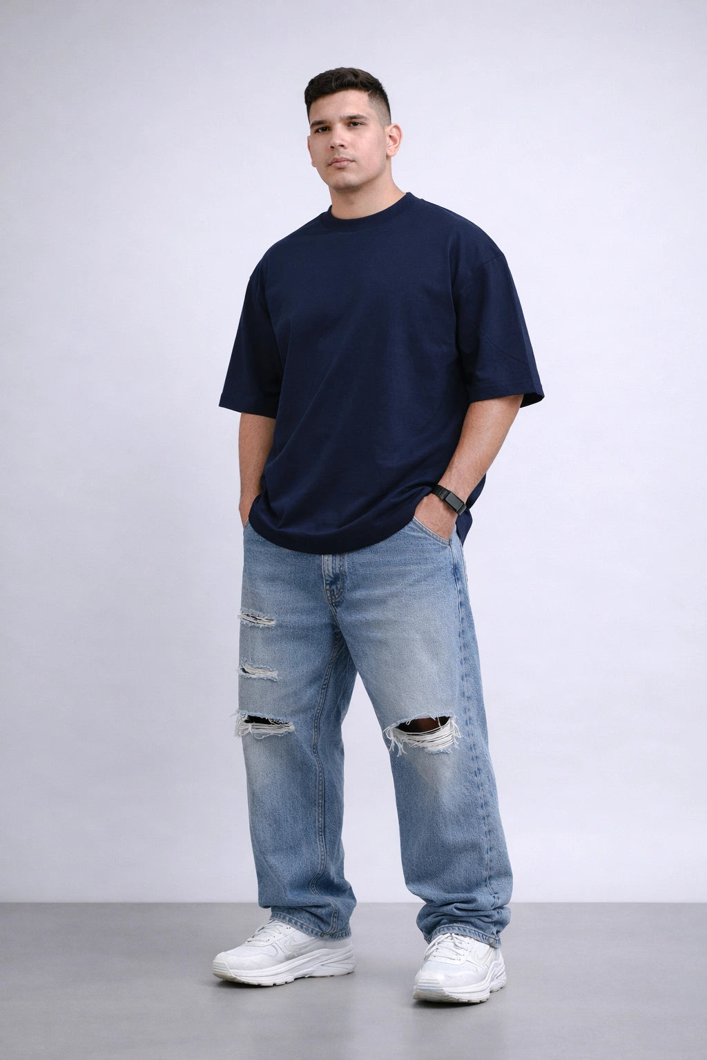 Man wearing a navy t-shirt and light blue jeans with a white background