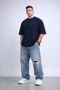 Man wearing a navy t-shirt and light blue jeans with a white background