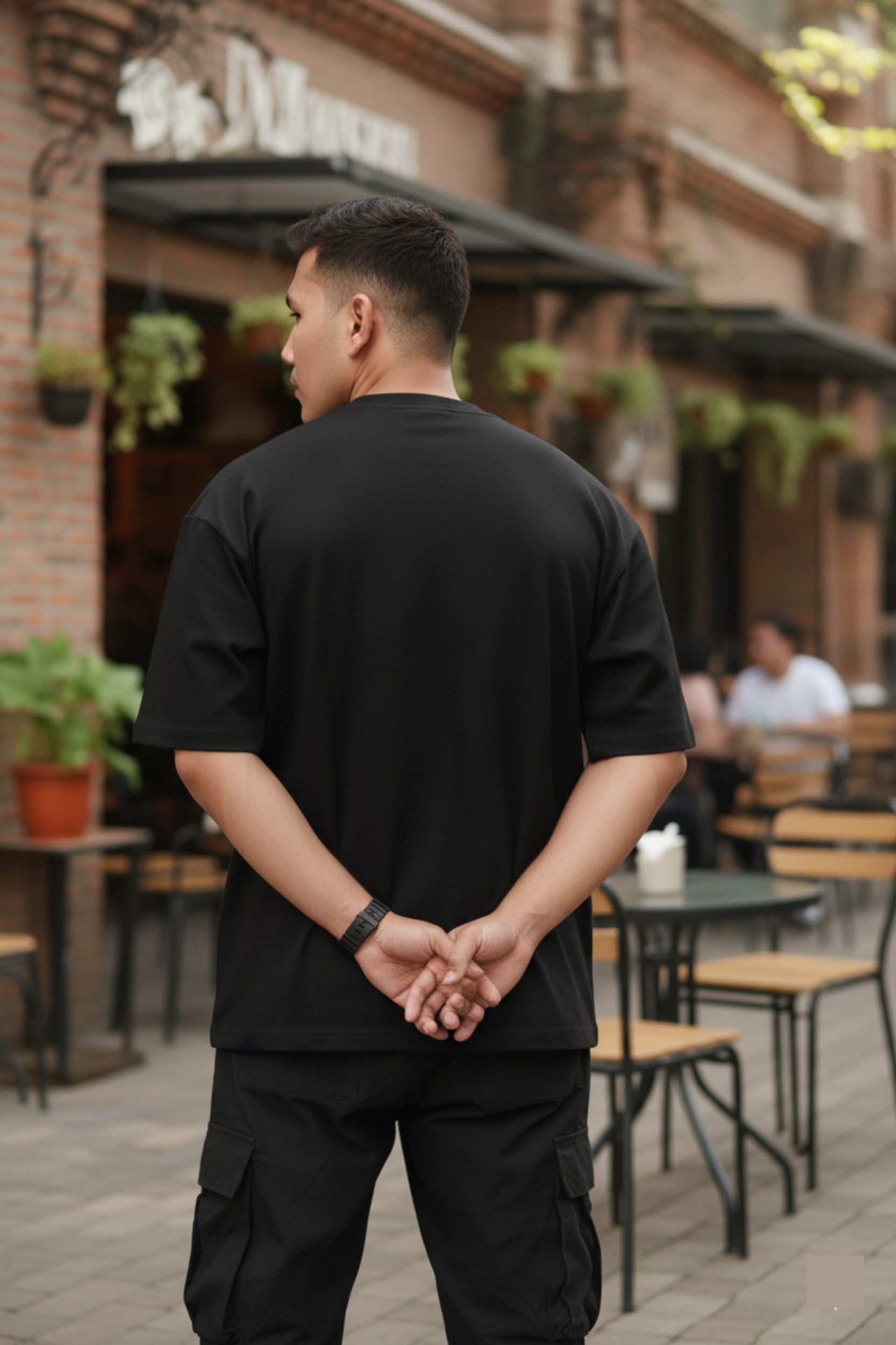 Man in a black outfit standing in an outdoor cafe setting