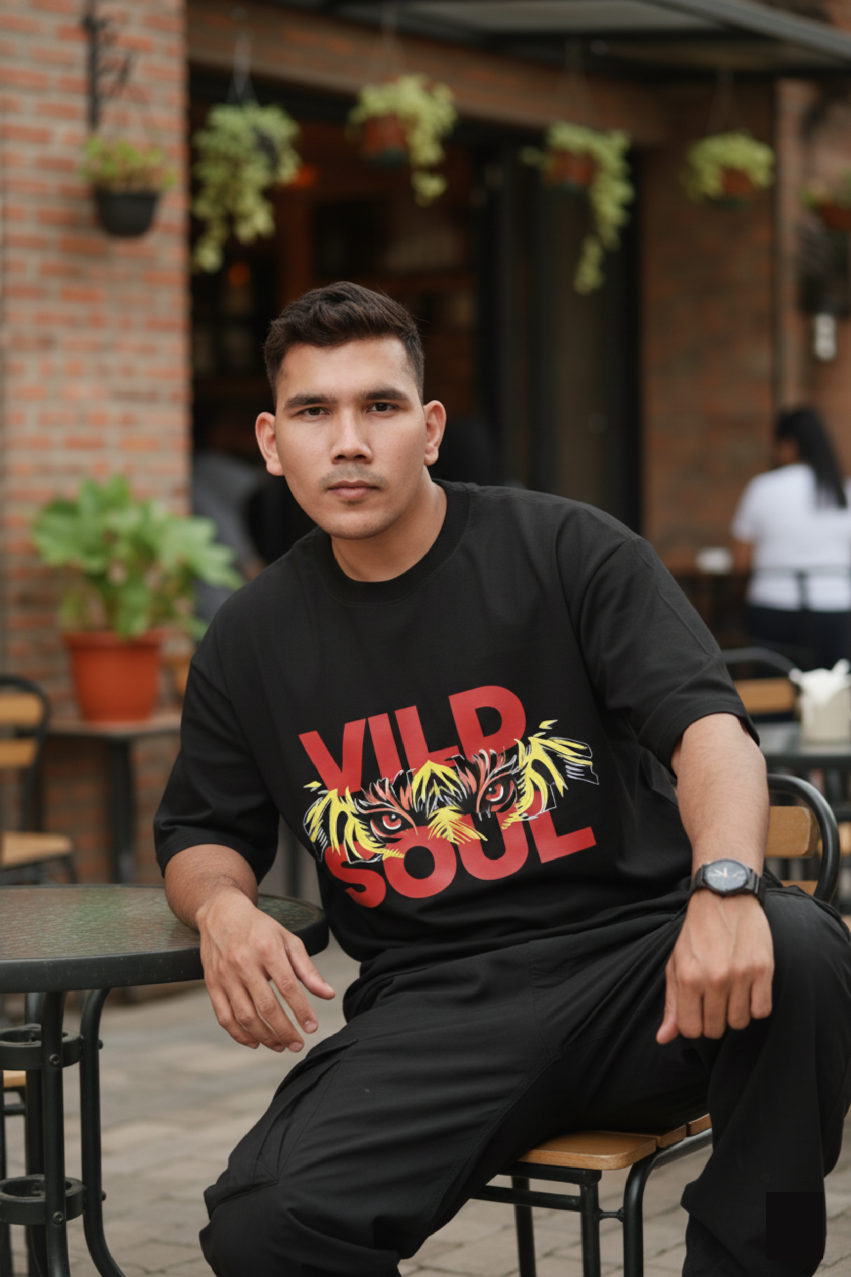Man wearing a black t-shirt with a colorful tiger design and 'Vild Soul' text, sitting outdoors.