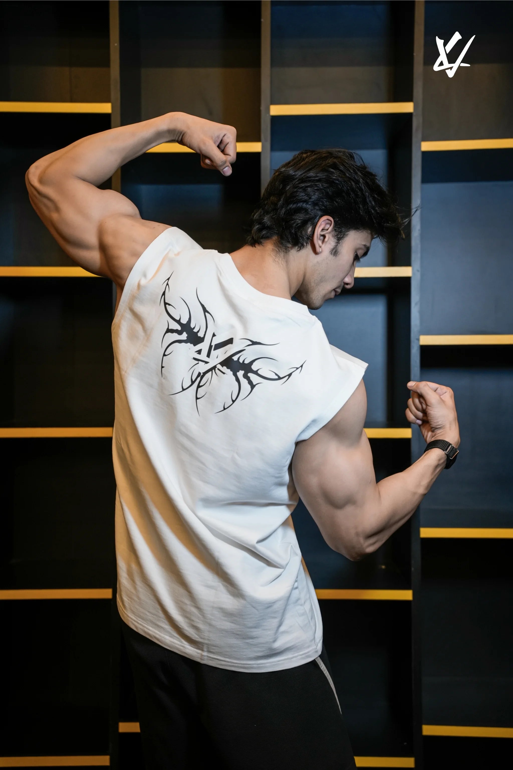 Man flexing his muscles wearing a white t-shirt with a black design in front of a dark background.