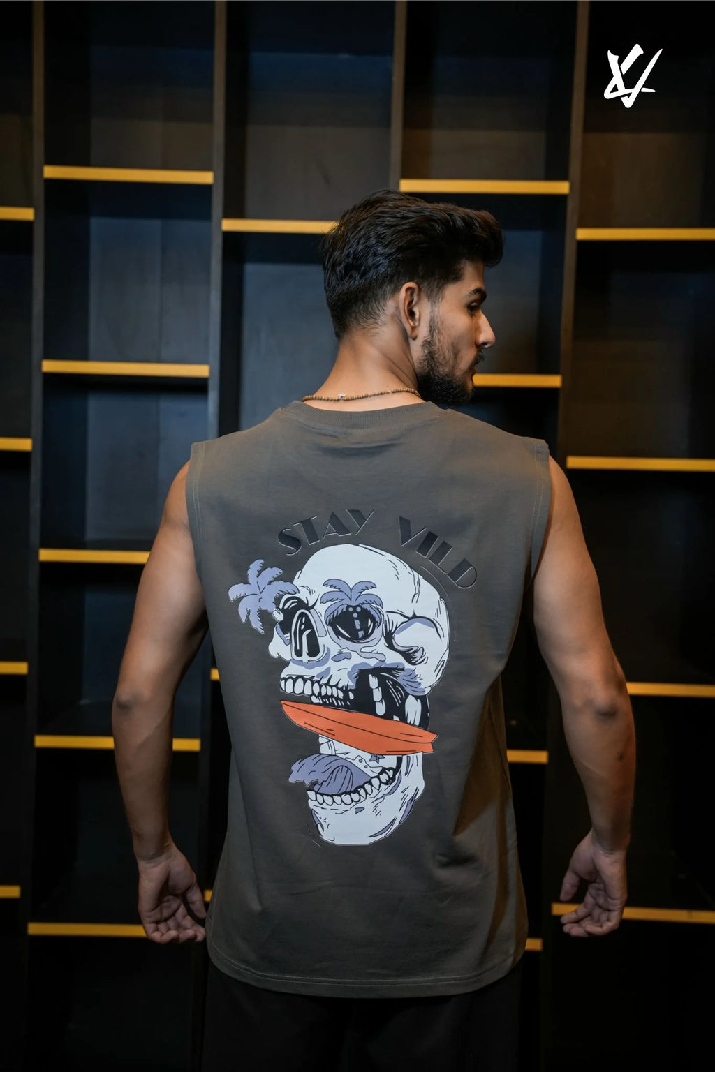 Man wearing a sleeveless shirt with a skull design on the back, standing against a dark background.