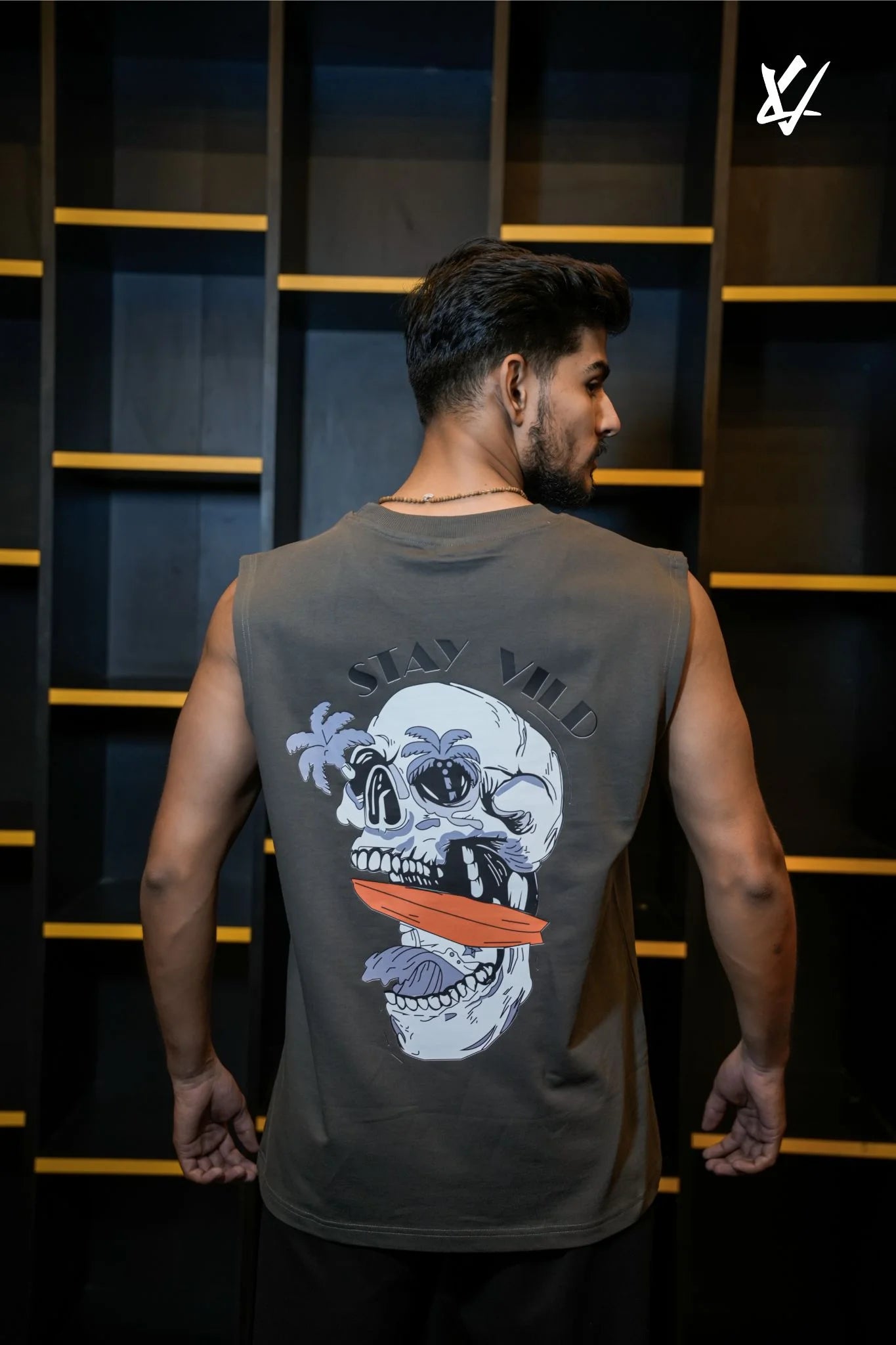 Man wearing a sleeveless shirt with a skull design on the back, standing against a dark background.