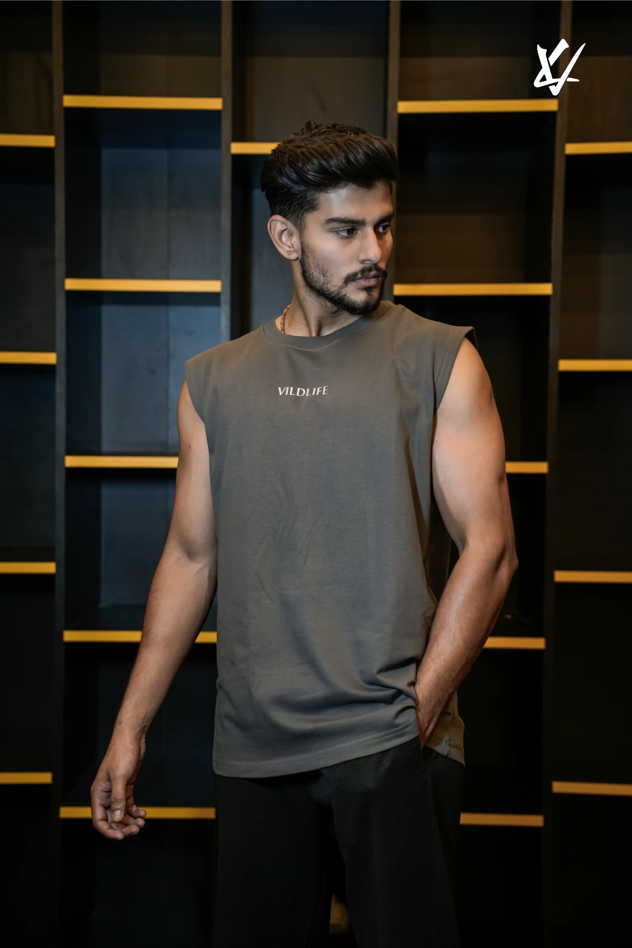 Man wearing a sleeveless gray shirt with a brand logo against a dark background